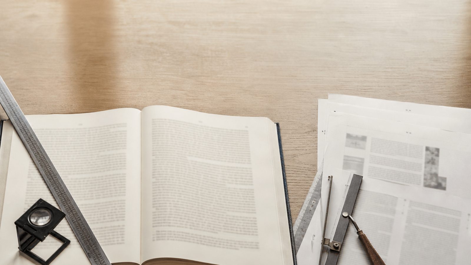Mesa de diagramação com livro aberto, régua tipográfica e provas de página